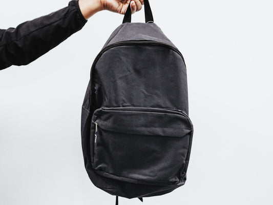 Leather backpack on a wooden desk next to a fabric backpack for comparison
